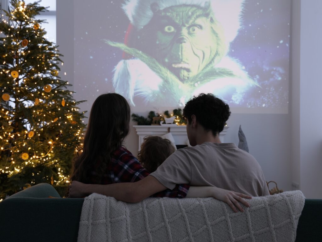 Eine Familie sieht über einen Beamer einen Weihnachtsfilm. Daneben steht ein Weihnachtsbaum.