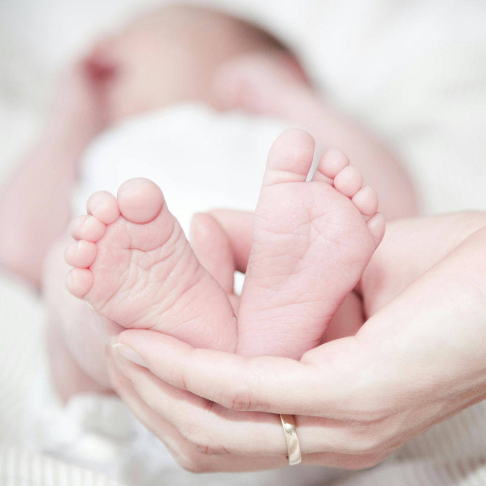 Glückwünsche zur Geburt: Auf dem Bild ist ein neugeborenes Baby. Im Vordergrund sind die Füße, die die Mutter in der Hand hält