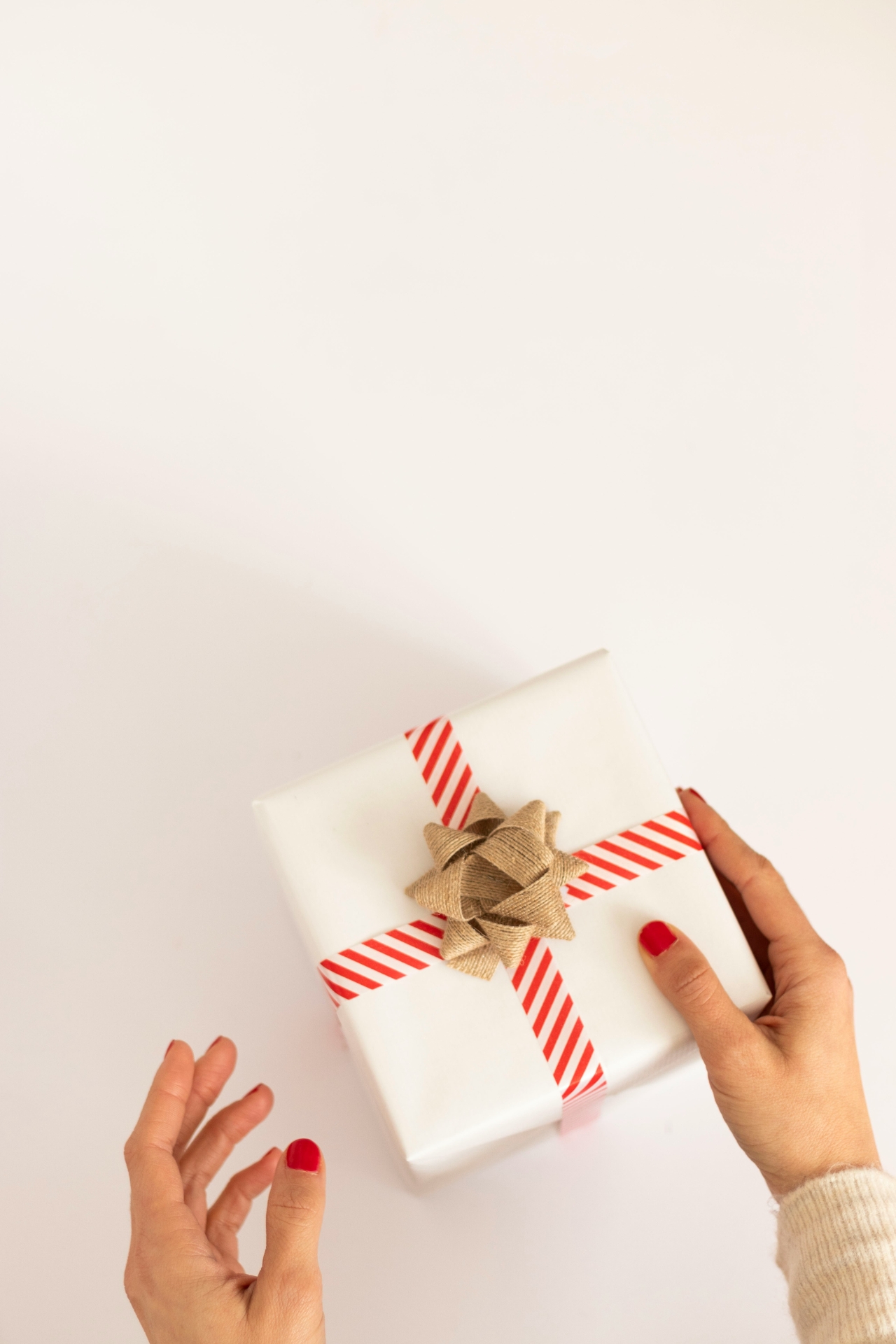 Last Minute Geschenke: Hände halten ein weißes Päckchen mit rotem Band und goldener Schleife