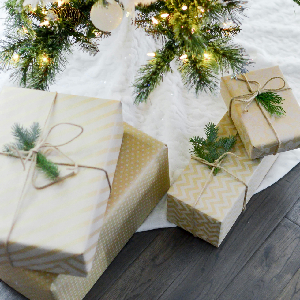 Auf dem Bild sind vier verpackte Geschenke unter einem Weihnachtsbaum mit Lichterketten