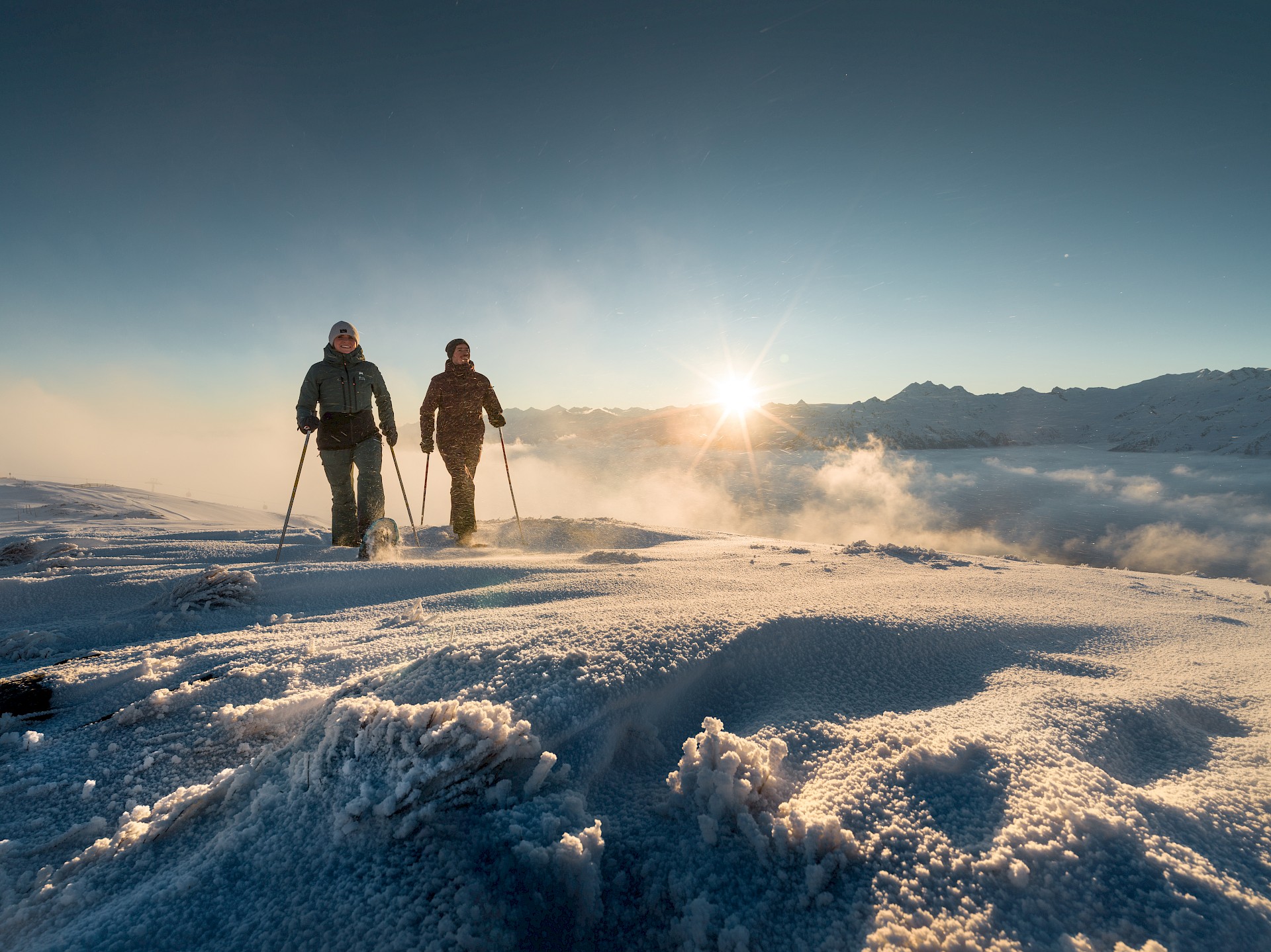 Skigebiet und Ferienregion Hohe Tauern, Wildkogel. Zwei Pistengeher im Schnee, im Hintergrund scheint die Sonne.