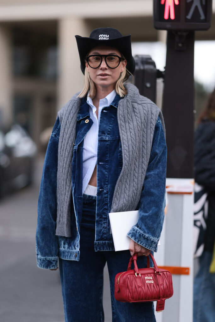 Constantly K: Interview mit Karin Teigl - am Bild: Karin Teigl mit roter miu miu Tasche, gestylt im Jeans-Look, schwarzem miu miu cowboy hut und schwarzer Brille, grauer Schal.