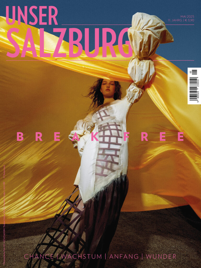 Mai Ausgabe 2025 / Unser Salzburg: Cover mit einer Frau die ihren linken, verbundenen Arm hochhält. Hinter ihr ein gelber Schleier. Titel: Break free