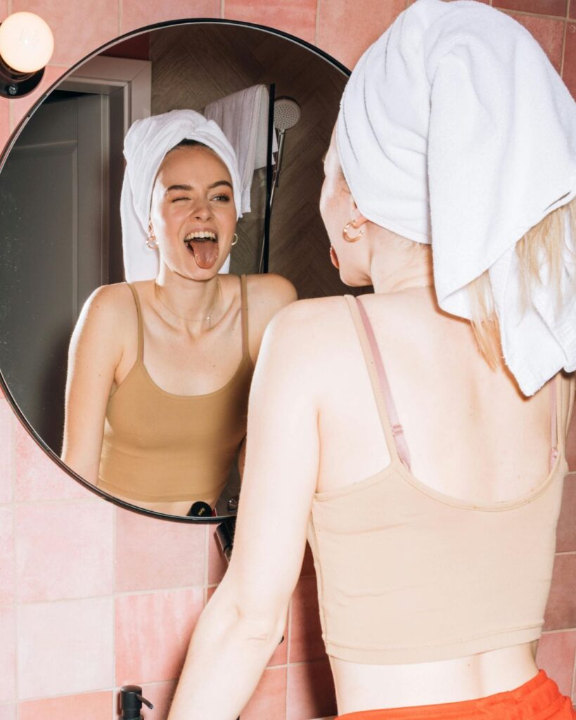 Wie sich Humor auf unsere Psyche auswirkt: Auf dem Bild ist eine Frau zu sehen, die in den Badespiegel schaut, zwinkert und die Zunge rausstreckt