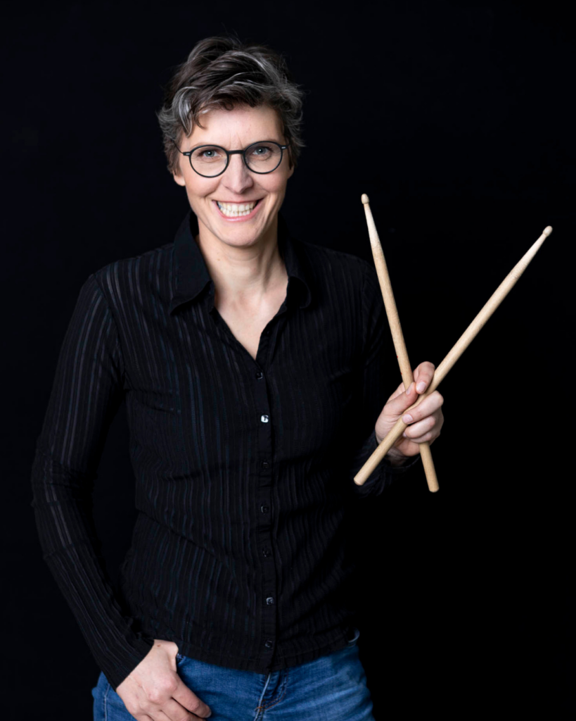 Elisabeth Fuchs: Die Dirigentin im Porträt mit zwei Drumsticks in der Hand.