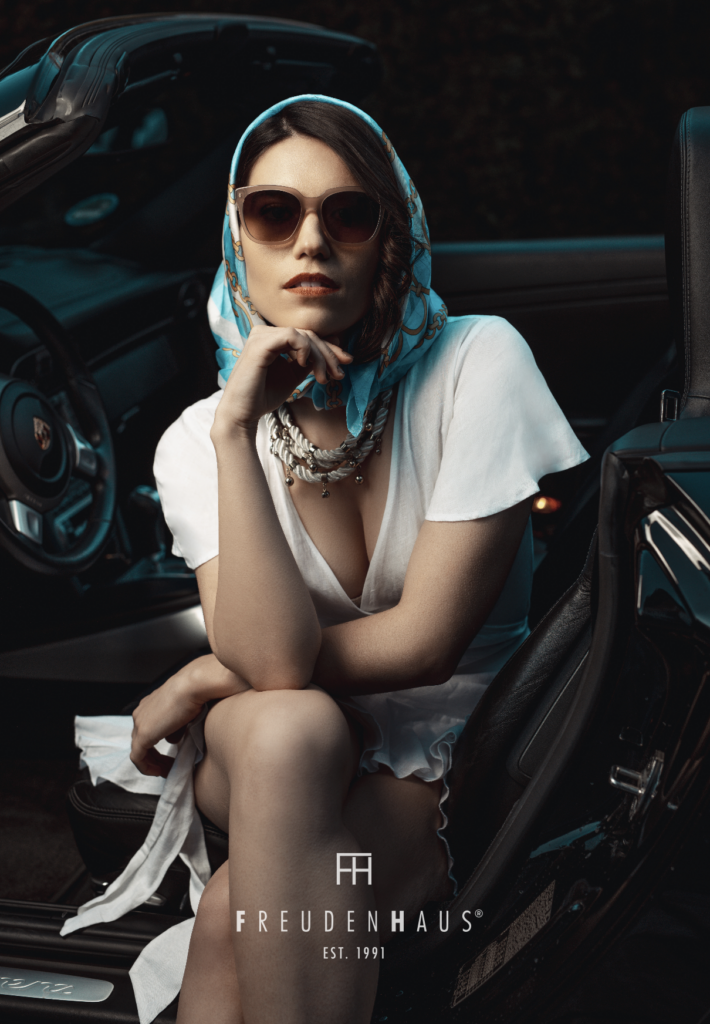 Brillenwerkstatt Roland Pföss: Neue Brillenkollektion. Auf dem Bild ist eine Frau mit Sonnenbrille zu sehen, die in einem Cabrio posiert