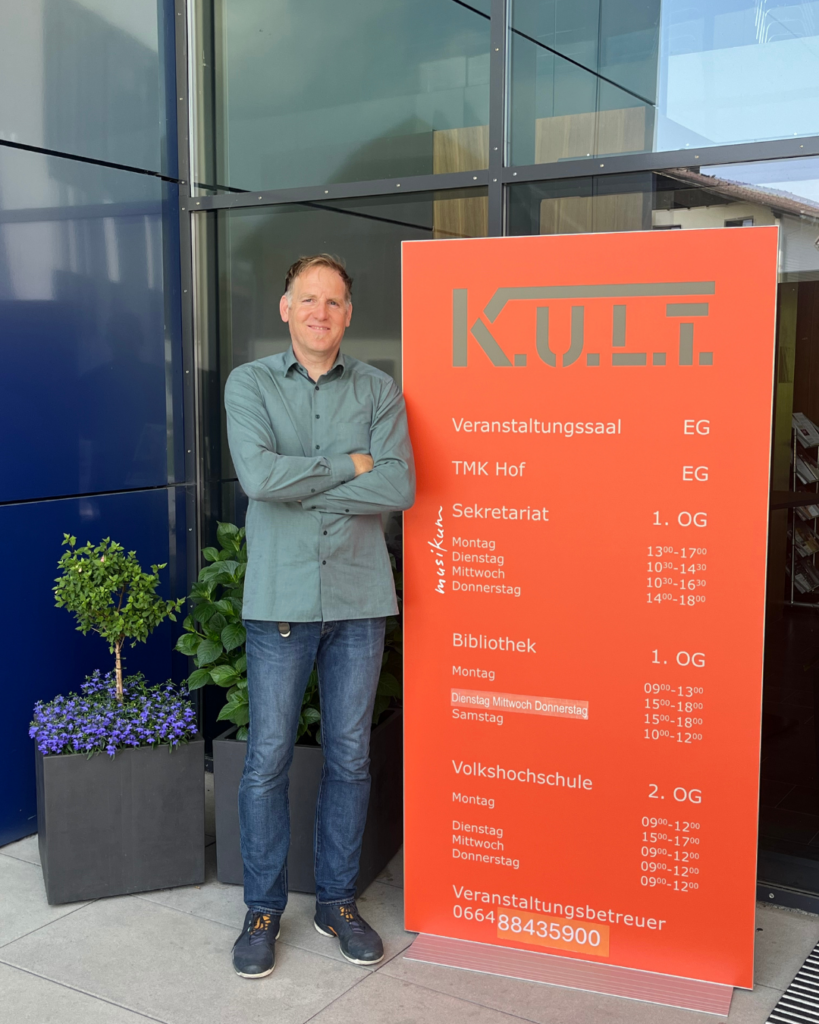Niclas Grundner, der Geschäftsführer von Kult in Hof vor einem roten Plakat mit den Öffnungszeiten des Kult.