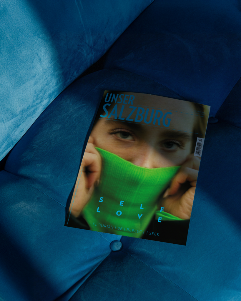 Unser Salzburg Cover November 2025, Frau, die sich grünen Rollkragenpulli über die Nase zieht