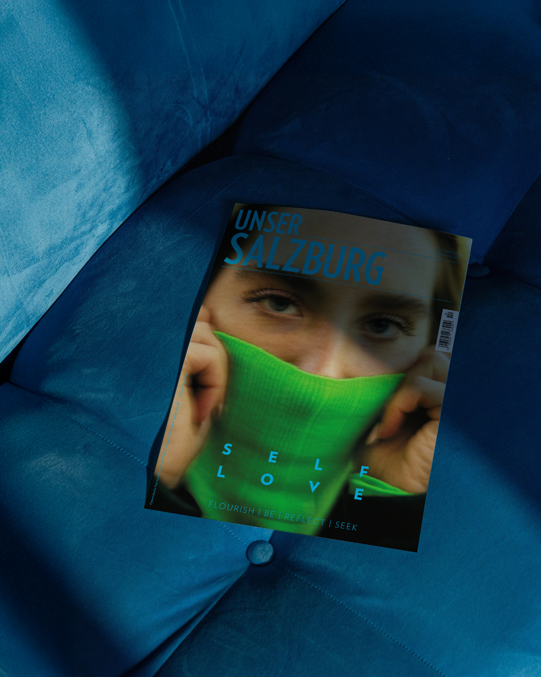 Unser Salzburg Cover November 2025, Frau, die sich grünen Rollkragenpulli über die Nase zieht