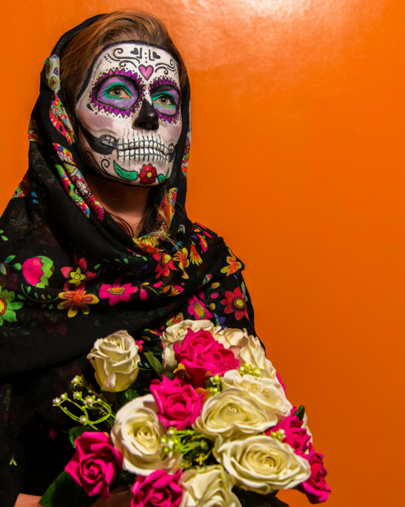 Mexikanisches Halloween: eine frau, die typisch mexikanisch zum Fest der Toten geschinkt ist, mit einem Rosenstrauß in der Hand