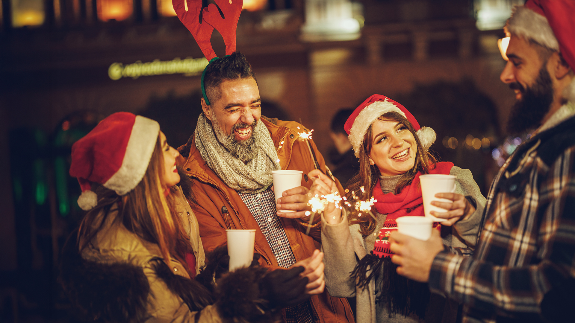 Adventmärkte: Freundesgruppe feiert mit heißen Getränken und Wunderkerzen am stimmungsvoll beleuchteten Markt.