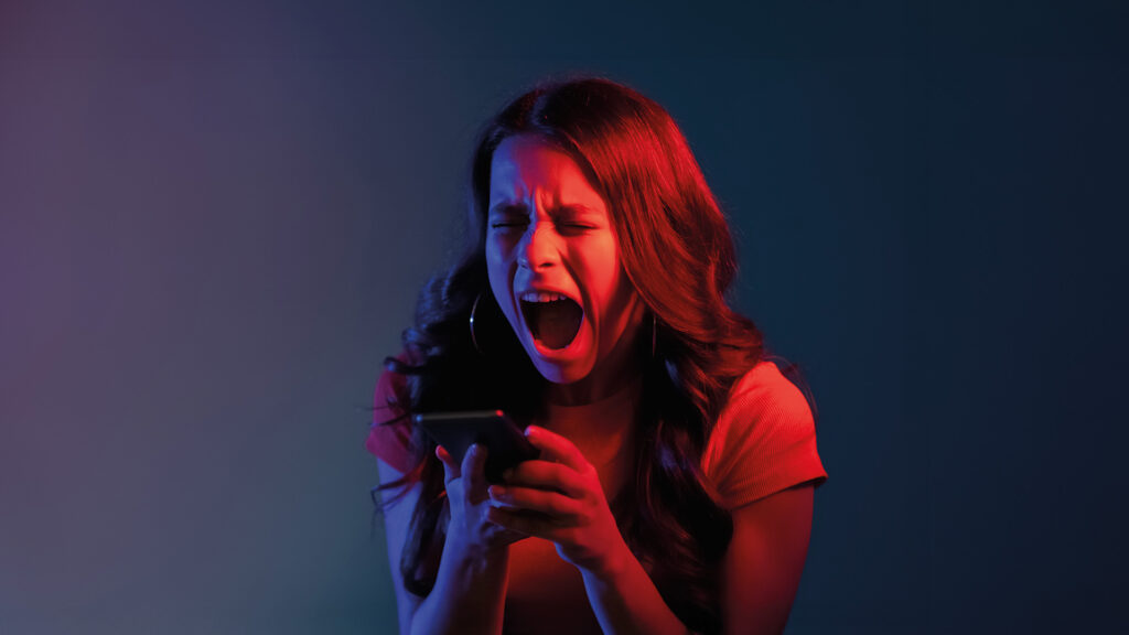 Cybergewalt: Frau schreit wütend in ein Smartphone, blau-rote Lichtstimmung.