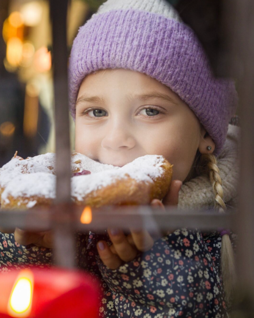 Ein kleines Mädchen mit lila Haube beißt in einen Krapfen