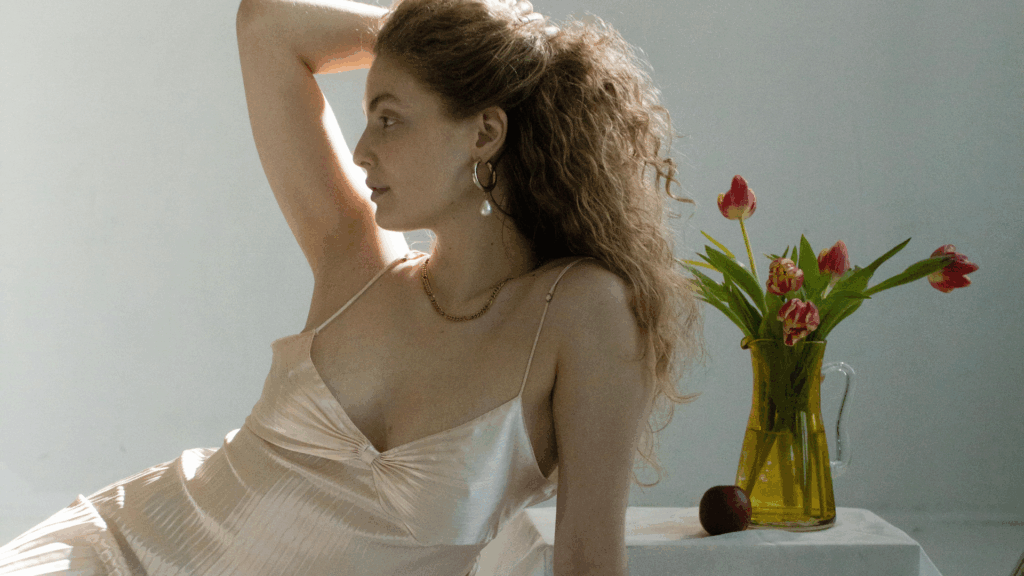 Eine Frau im Slipdress greift sich seitlich in die Haare, daneben steht ein Tulpenstrauß