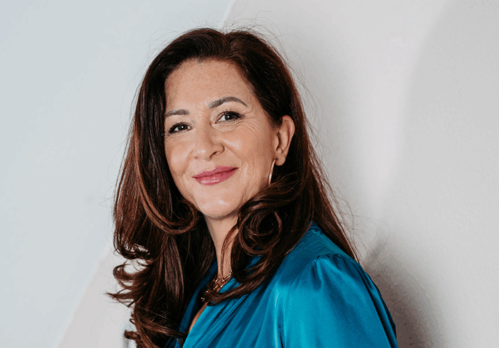 Autorin Ute Zischinsky in blauem Satin-Oberteil, hält eine Tasse in der Hand und lächelt in die Kamera