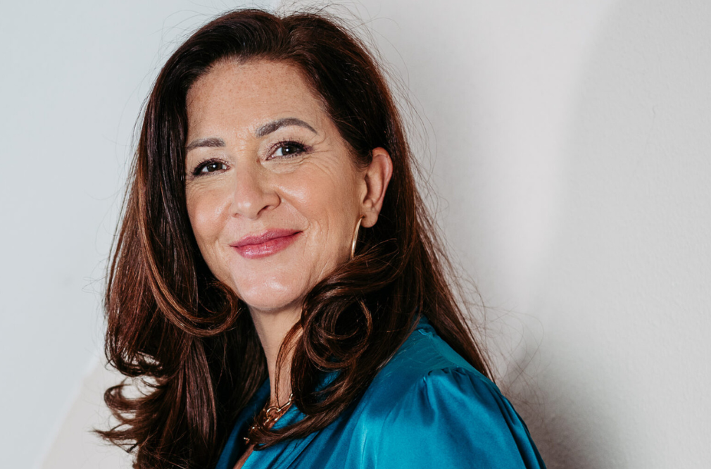 Autorin Ute Zischinsky in blauem Satin-Oberteil, hält eine Tasse in der Hand und lächelt in die Kamera