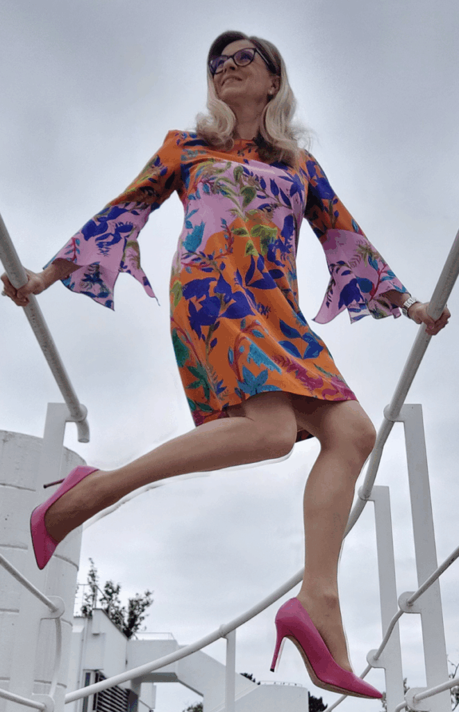 Christa Kummer springt - buntes Kleid und pinke High Heels