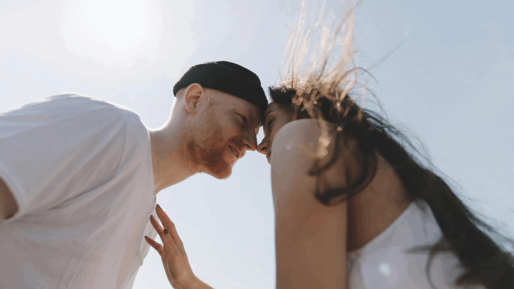 Ein Mann und eine Frau sind mit ihren Gesichter nah beieinander unter blauem Himmel
