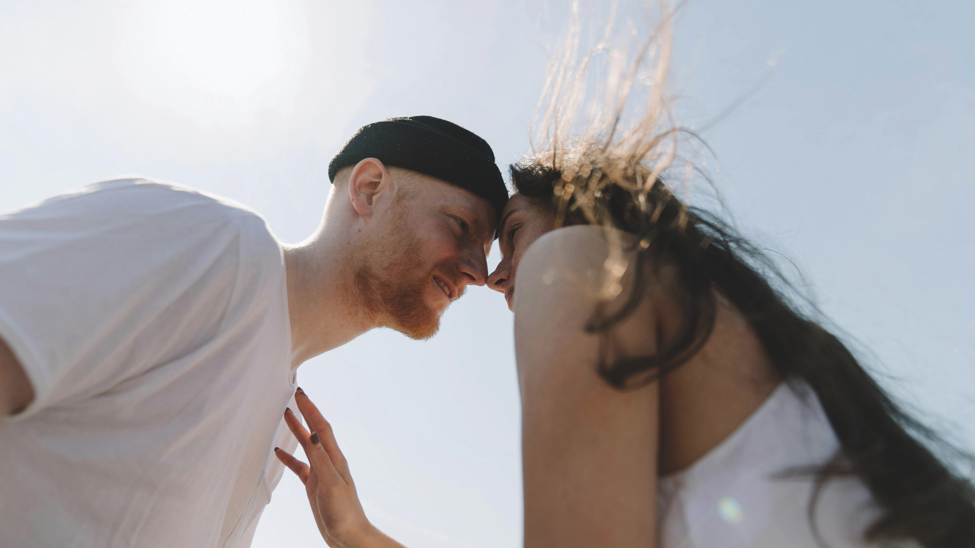 Ein Mann und eine Frau sind mit ihren Gesichter nah beieinander unter blauem Himmel