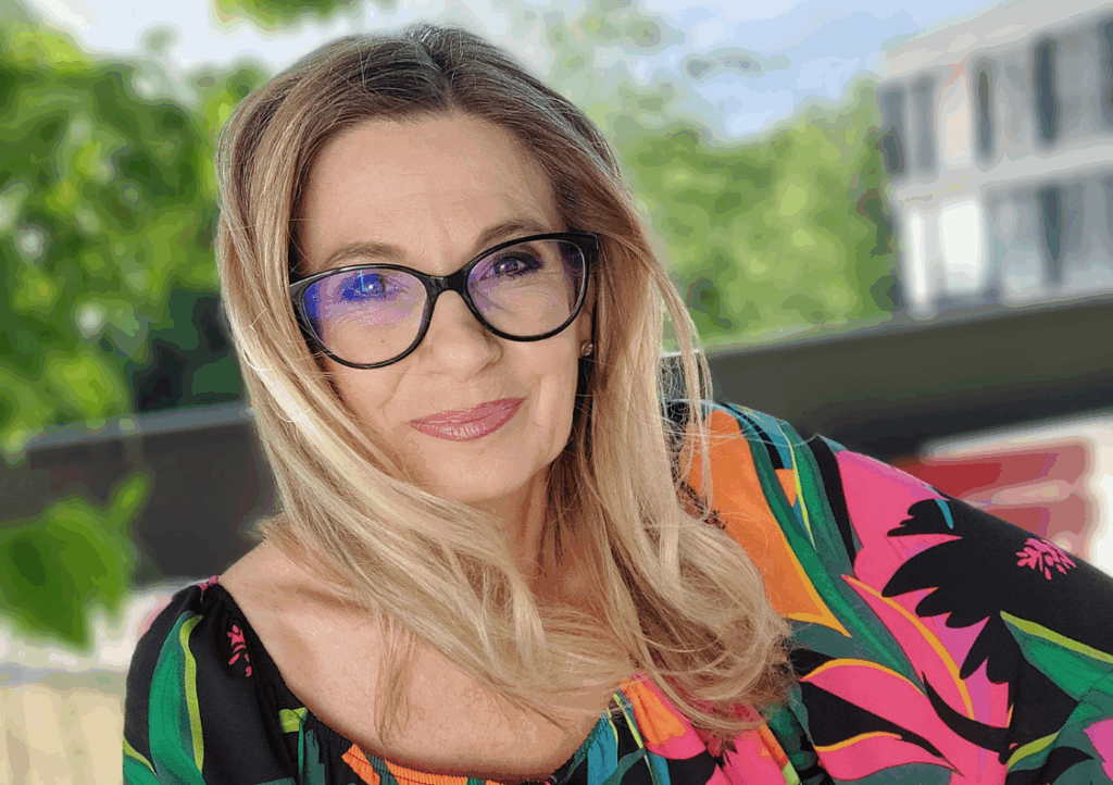 Christa Kummer im Portrait: Mit bunter Bluse und Brille, sieht in die Kamera
