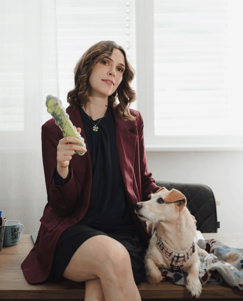 Eine Dame mit einer Gurke in der Hand und rechts von ihr ein Hund