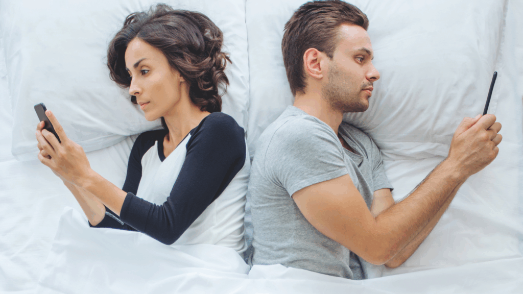 Liebe, Lust und Likes: Paar liegt mit dem Rücken zueinander gedreht im Bett und schauen jeweils auf das Handy